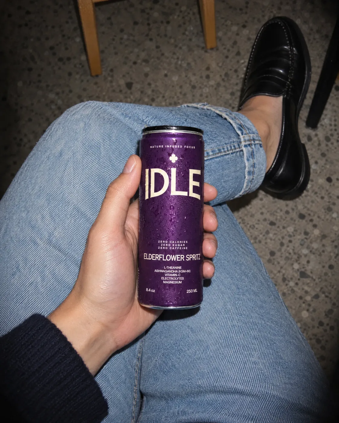 An IDLE Elderflower Spritz can held over a knee in blue jeans