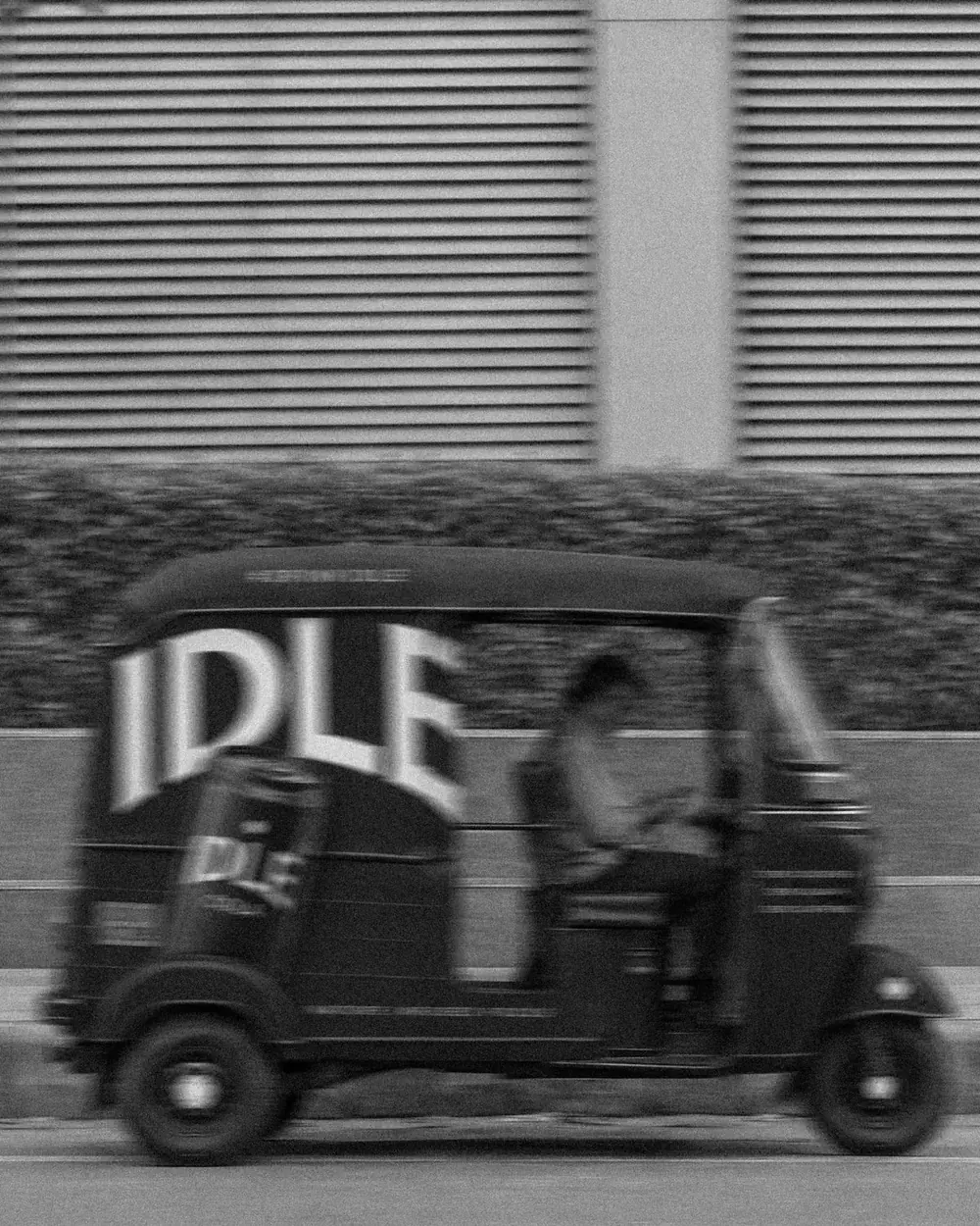 A black auto-rickshaw with the IDLE wordmark, blurred in motion
