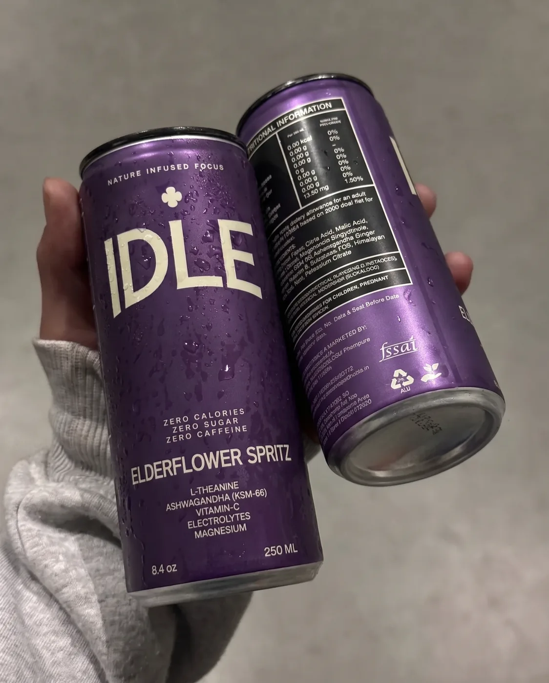 Two cold IDLE Elderflower Spritz cans in one hand, front and nutrition label