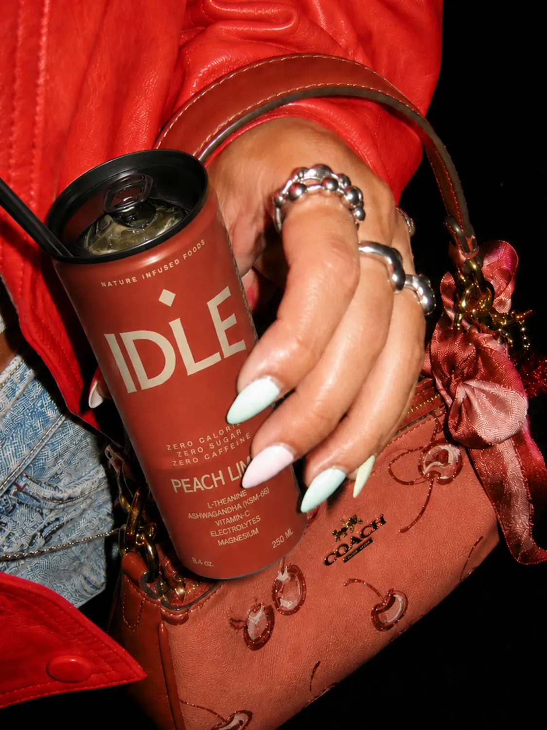 A hand with rings holding a Peach Lime can by a red bag